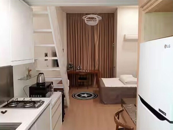 Una habitación de hotel compacta con kitchenette, una cama, una mesita y una silla.