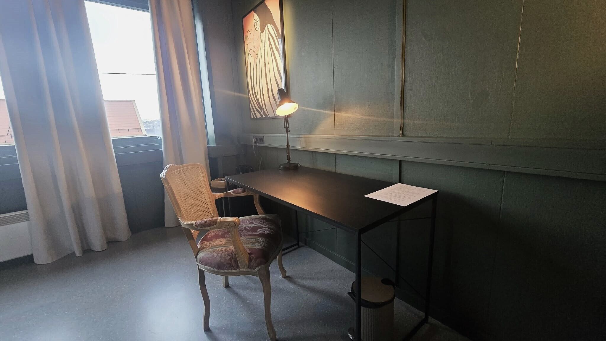 A room with a desk, chair, lamp, and a painting on the wall.