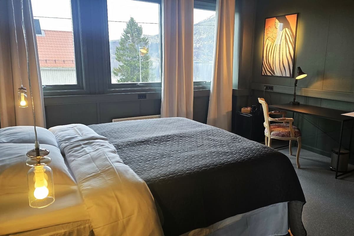 A hotel room with a bed, a desk, a chair, a lamp, and a painting on the wall.