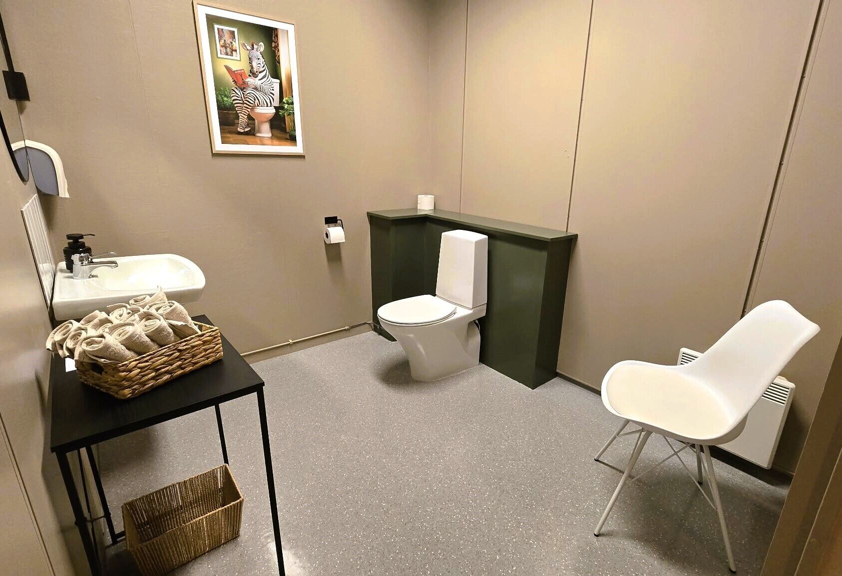 Un baño pequeño con inodoro, lavamanos, una silla y una cesta de toallas.