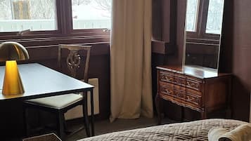 A hotel room with a bed, a desk, a chair, a dresser, and a large window with curtains.
