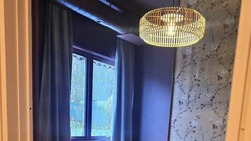 A bedroom with a bed, a nightstand, a dresser, a chair, and a hanging light fixture.