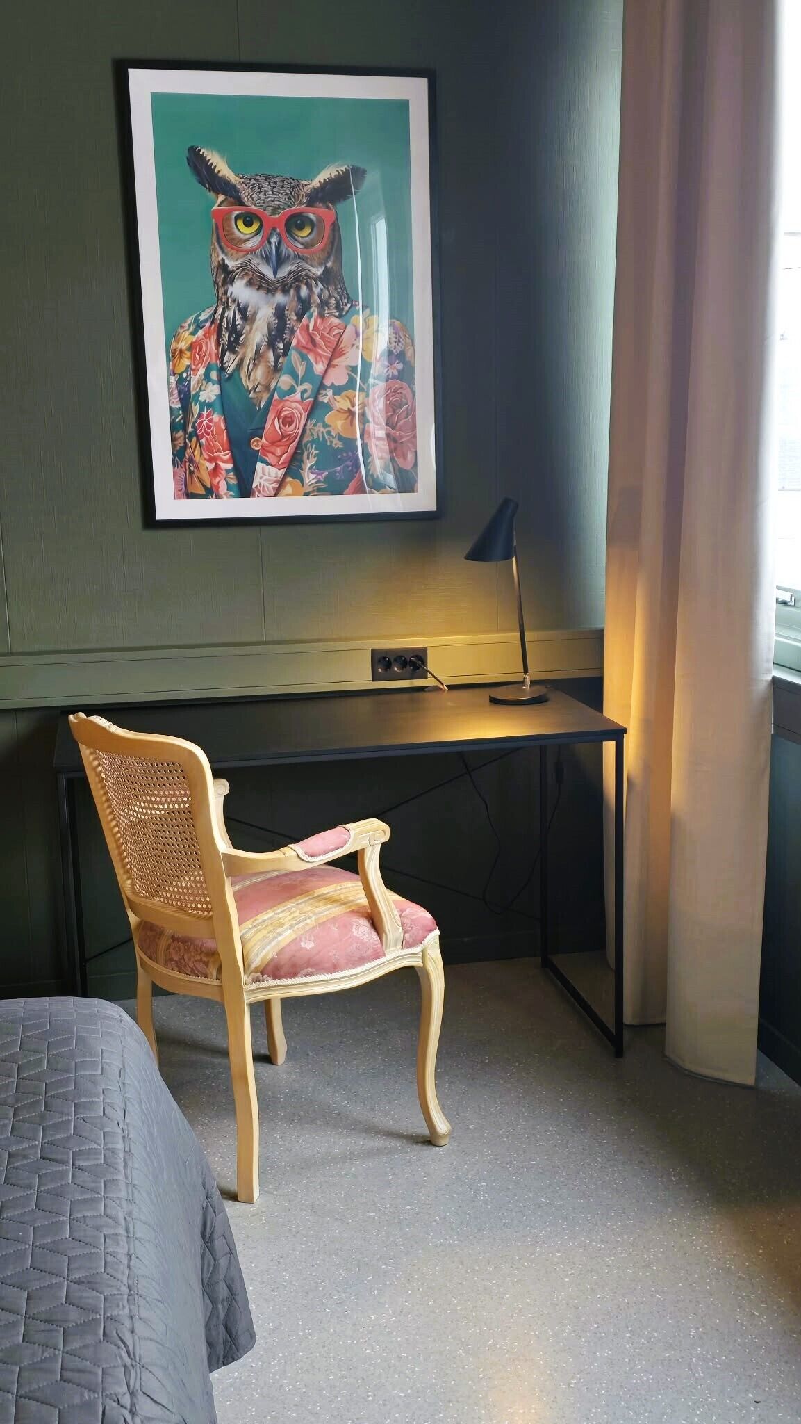 A room with a desk, a chair, a framed artwork of an owl, and a lamp.