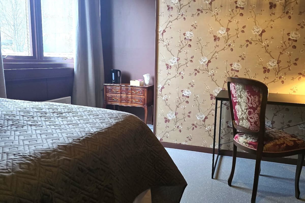 A hotel room with a bed, a desk with a lamp, a chair, and a dresser.