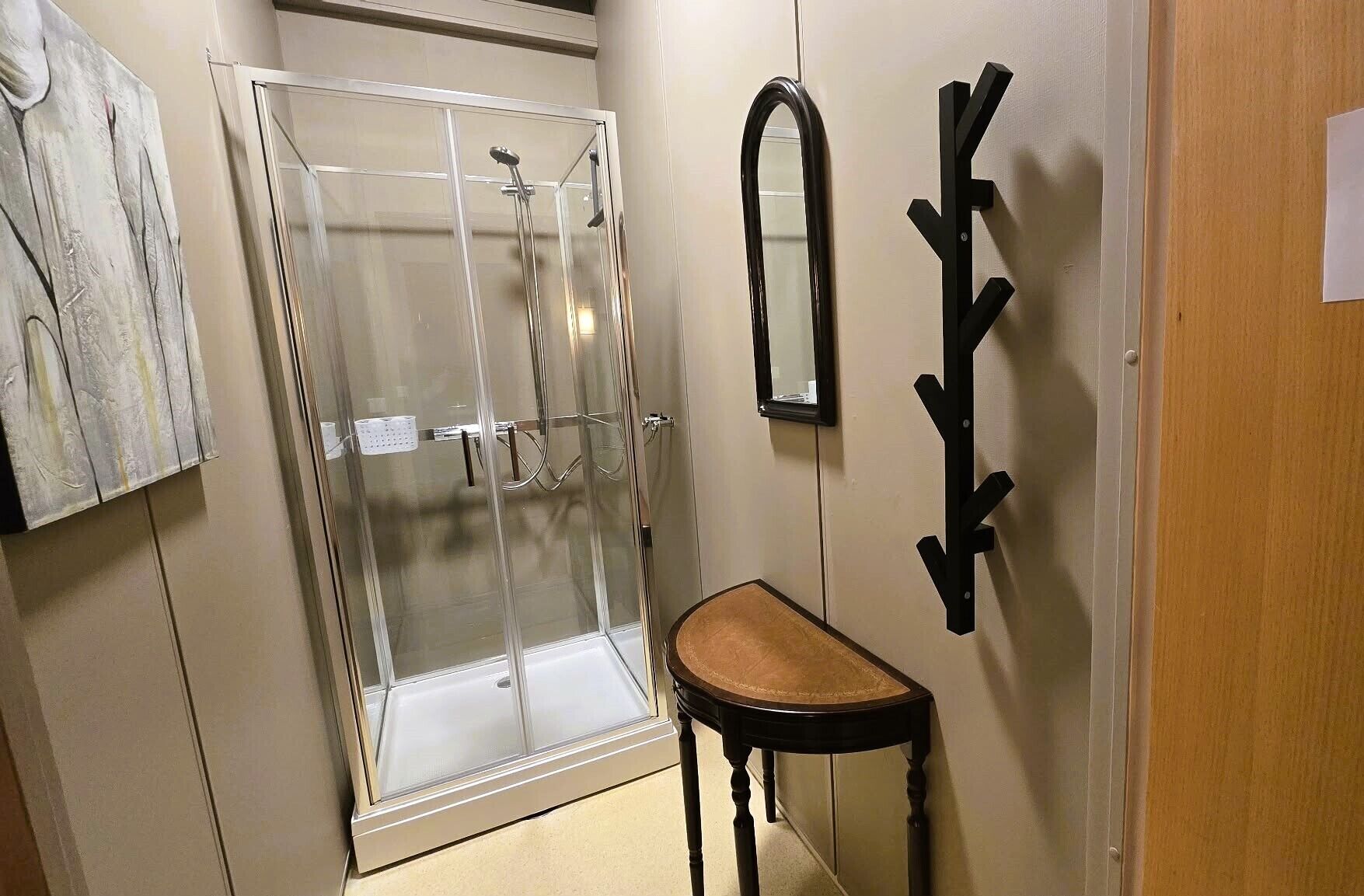 Un baño con cabina de ducha de vidrio, un banco de madera, un espejo montado en la pared y un perchero para toallas.