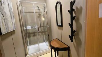 Un baño con cabina de ducha de vidrio, un banco de madera, un espejo montado en la pared y un perchero para toallas.