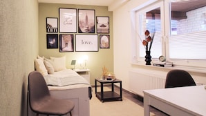 A compact hotel room with a bed, a small table, a chair, and a window with a view of the city. - Cozy one-room apartment in Hagen a.T.W. (long-stay) (Hagen am Teutoburger Wald)
