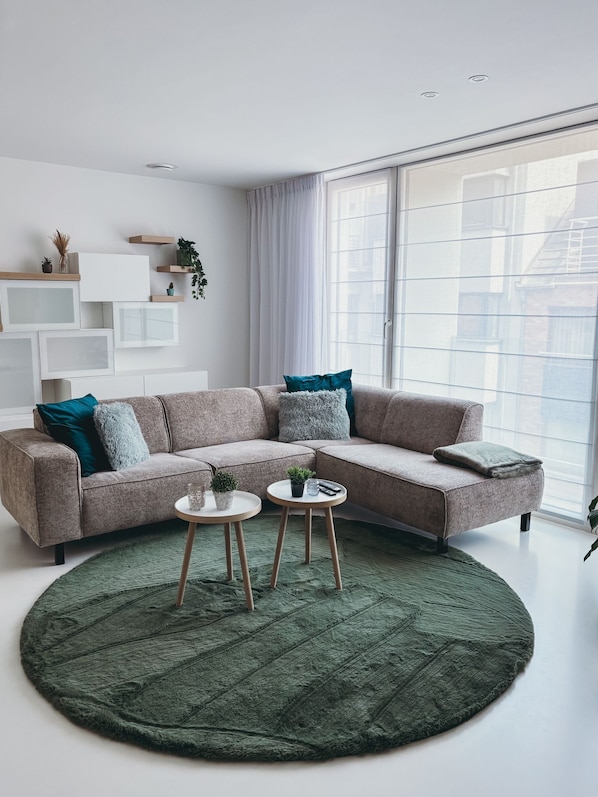 A modern living room with a large window, a sectional sofa, a round rug, and a small coffee table.