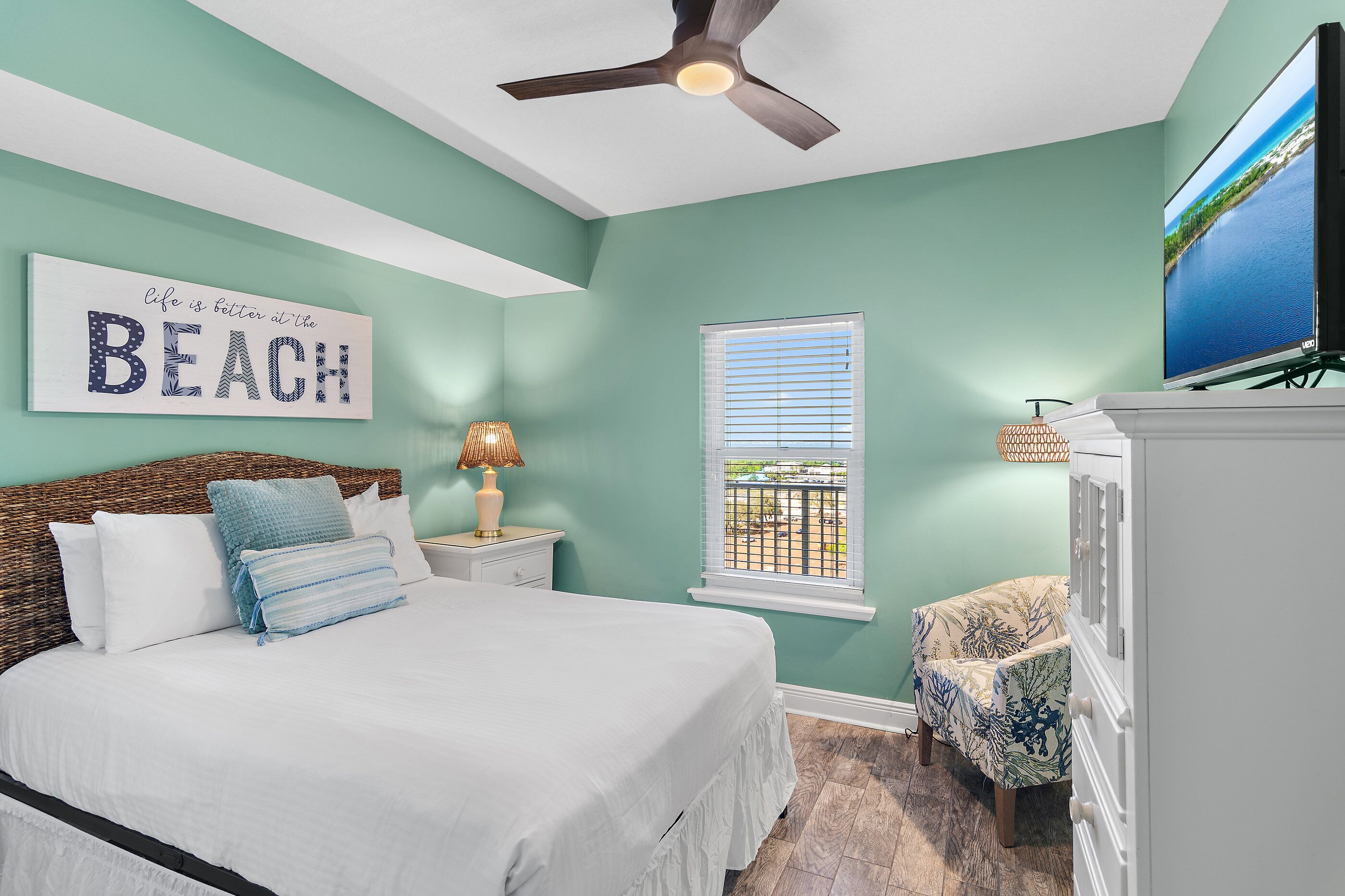A bedroom with a bed, a ceiling fan, a TV, a window, and a wall sign.