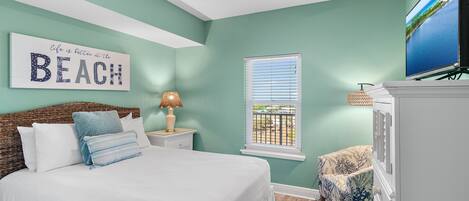 A bedroom with a bed, a ceiling fan, a TV, a window, and a wall sign.