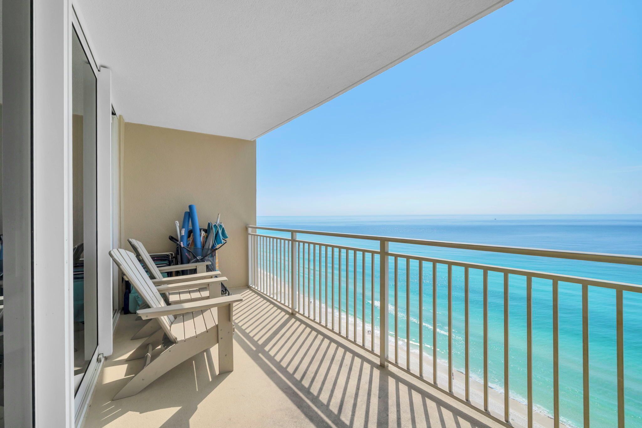 A balcony with a view of the ocean, a railing, and a few chairs.