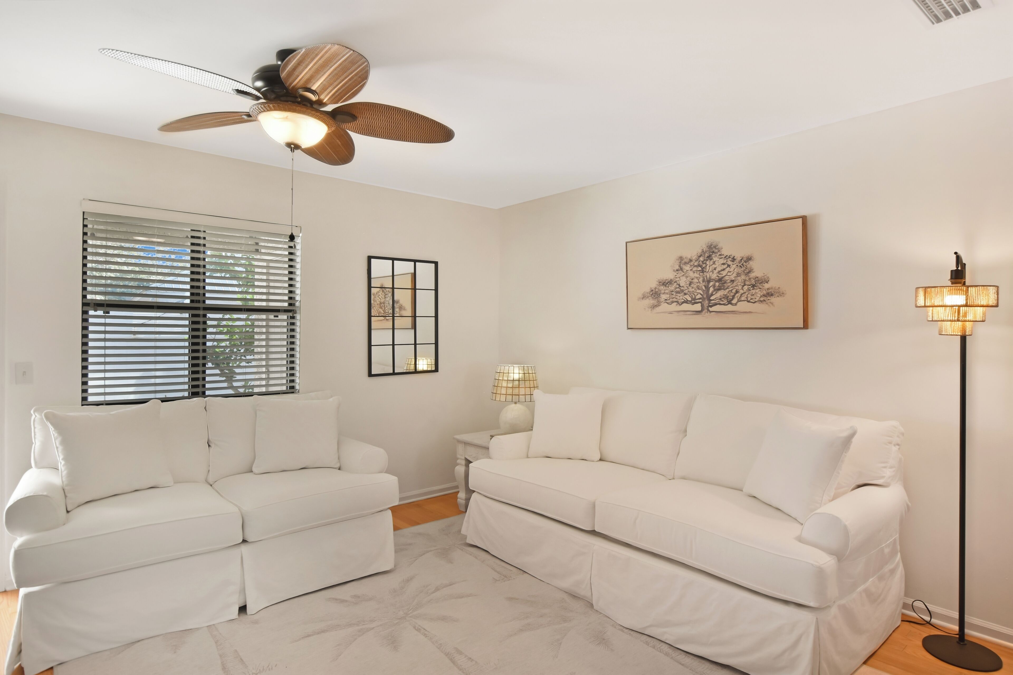 Un salon moderne avec un canapé blanc, un ventilateur de plafond, une lampe sur pied et un tableau encadré accroché au mur.