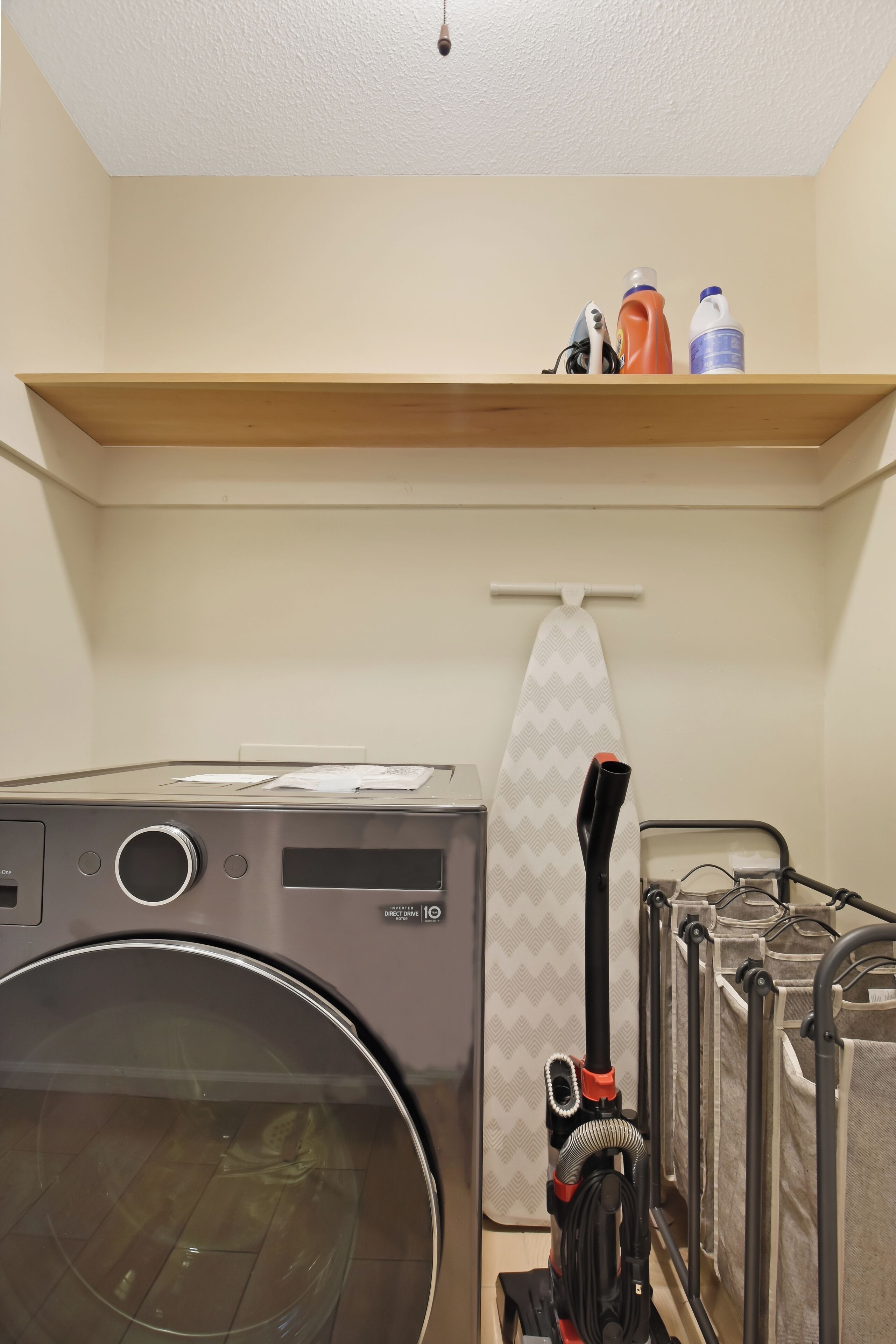 A laundry area with a washing machine, a vacuum cleaner, and a shelf with cleaning supplies.
