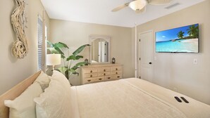 A bedroom with a bed, a dresser, a ceiling fan, a TV displaying a beach scene, and a plant. - 2 Bedroom 1.5 Bath Townhouse.  Close to Beach and the Pier/Village area. (Saint Simons Island)