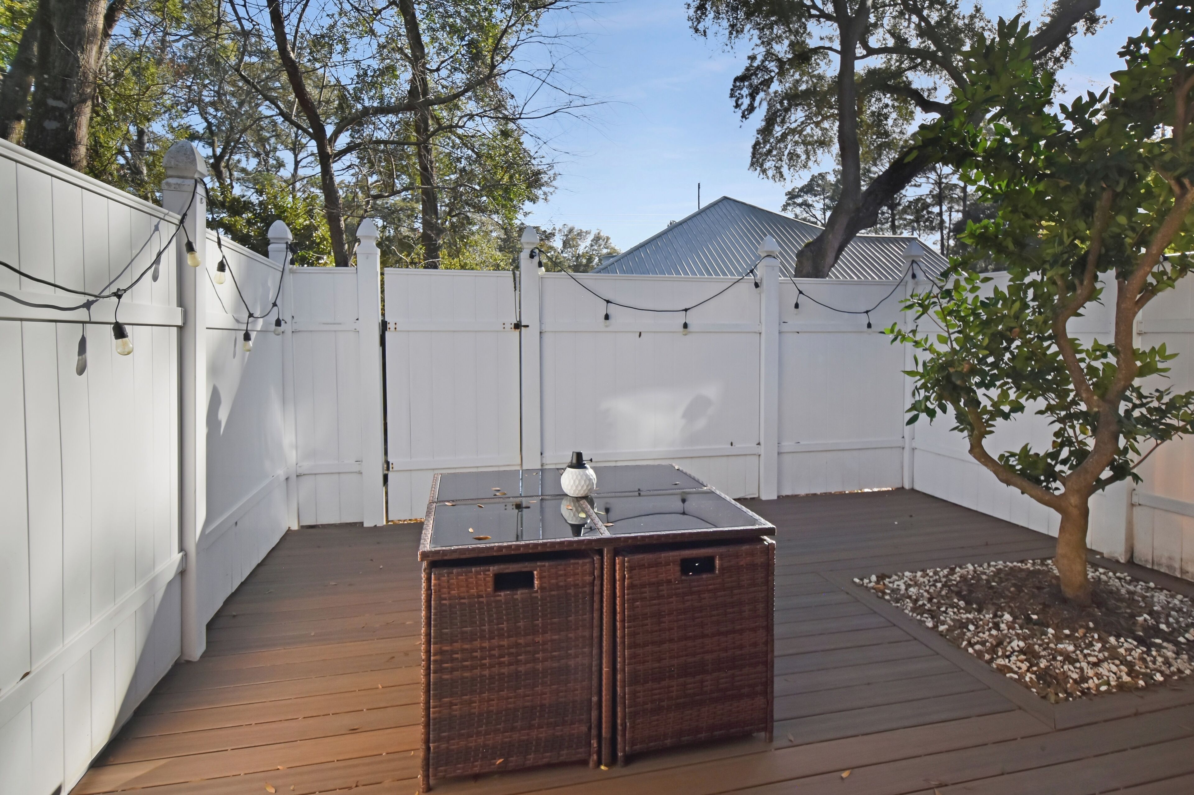 Une terrasse en bois avec une table à plateau de verre et un petit arbre.
