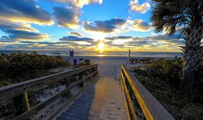 Una passerella in legno che conduce alla spiaggia, con un tramonto sullo sfondo.