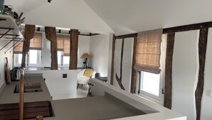 Ein modernes Loft mit freiliegenden Holzbalken, einer Küchenzeile mit Wasserkocher und einer gemütlichen Sitzecke mit einer Lampe.