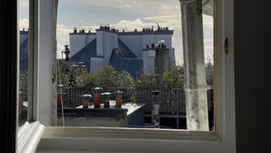 Blick durch ein Fenster eines Gebäudes mit moderner Architektur, das einen markanten Schornstein und einen Metallzaun im Vordergrund zeigt.
