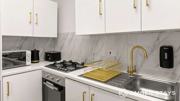 Una cocina moderna con armarios blancos, detalles dorados, una estufa a gas, un lavamanos y un escurreplatos.
