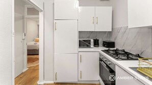 Cocina compacta con armarios blancos, un microondas, estufa y pileta.