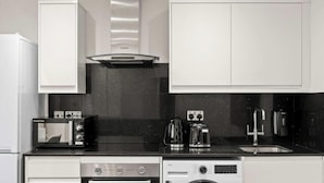 Een moderne keuken met witte kasten, een zwart aanrecht, een ingebouwde oven, een koffiezetapparaat en een spoelbak.