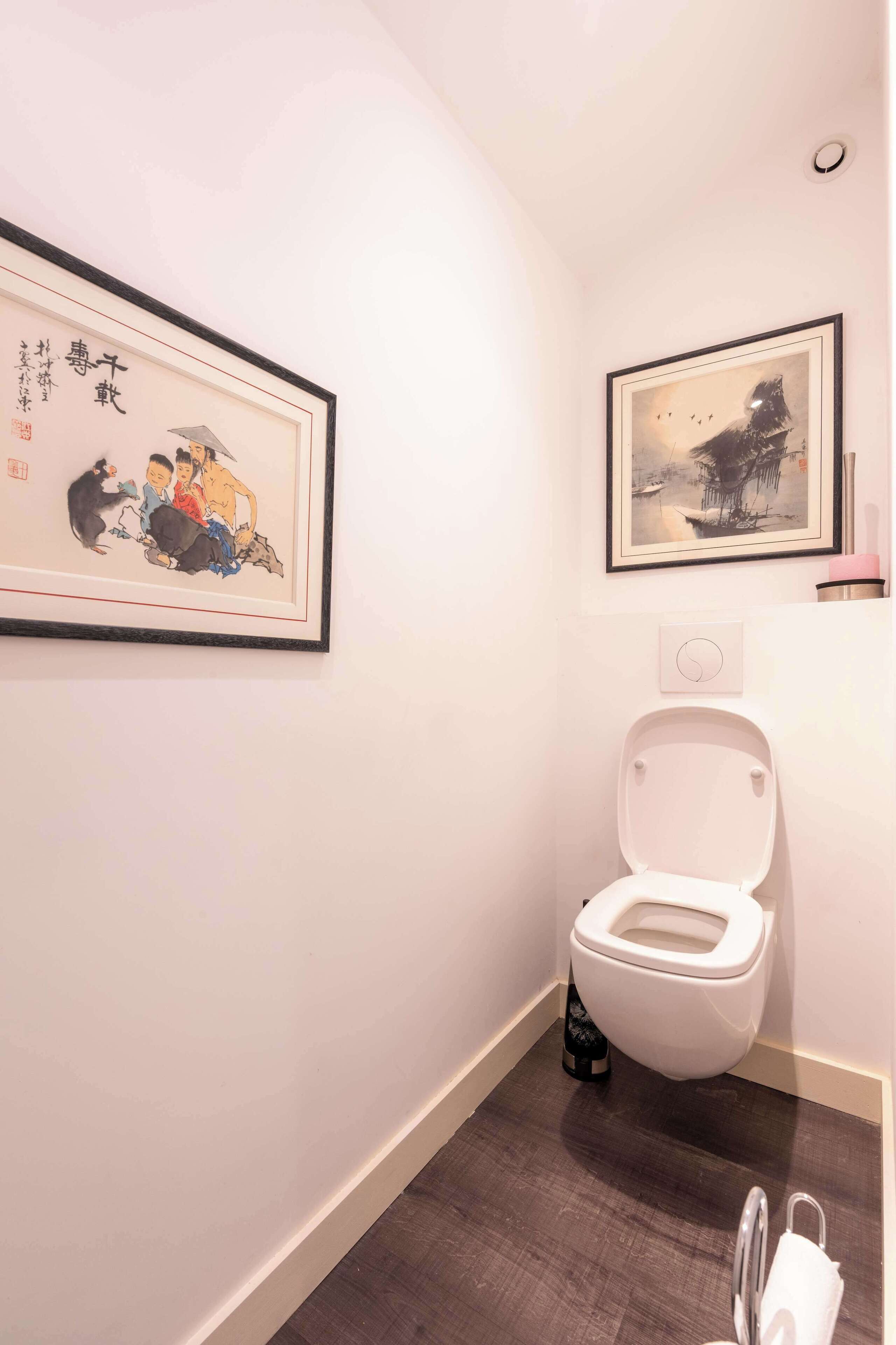 Een badkamer met een toilet, een fotolijst aan de muur en een vloermat.