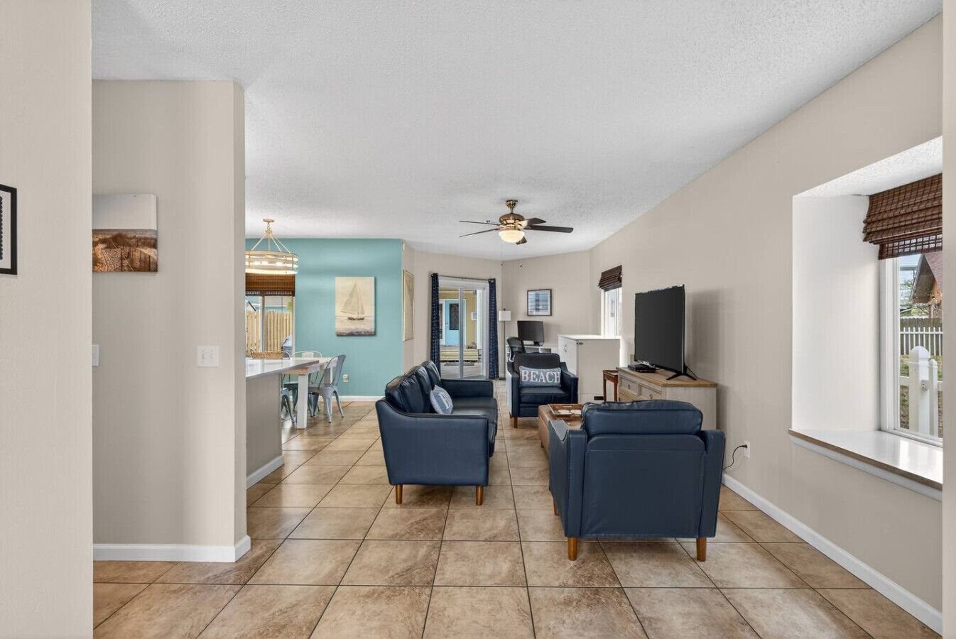 A spacious living room with a large TV, a ceiling fan, and a view of the backyard through a window.