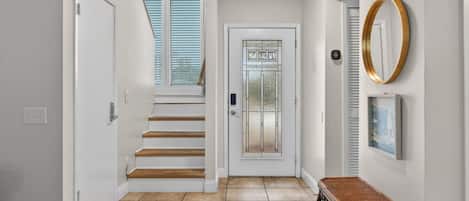 A hallway with a staircase, a door with a glass panel, a wall-mounted mirror, and a small table.