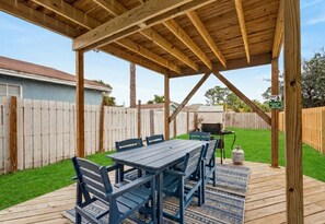Een houten terras met een overdekte patio, een tafel met stoelen en een barbecue.