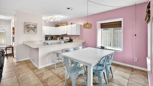 A modern kitchen with white cabinets, a central island, and a dining area with blue chairs. - Emerald Escape 1 - 3 Blocks to Beach (Panama City)
