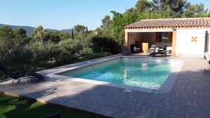 A swimming pool with a tiled deck, surrounded by greenery and a building with outdoor seating. - 3-bedroom villa with exclusive pool (Garéoult)