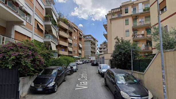 Une rue étroite bordée d’immeubles résidentiels à plusieurs étages, de voitures garées et d’un panneau indiquant la « Via Cingoli ».