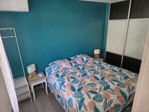 A bedroom with a teal wall, a bed with a leaf-patterned bedspread, a bedside table with a lamp, and a white wardrobe. - 2-4 person 2* cottage in sought-after neighborhood (Sanary-sur-Mer)