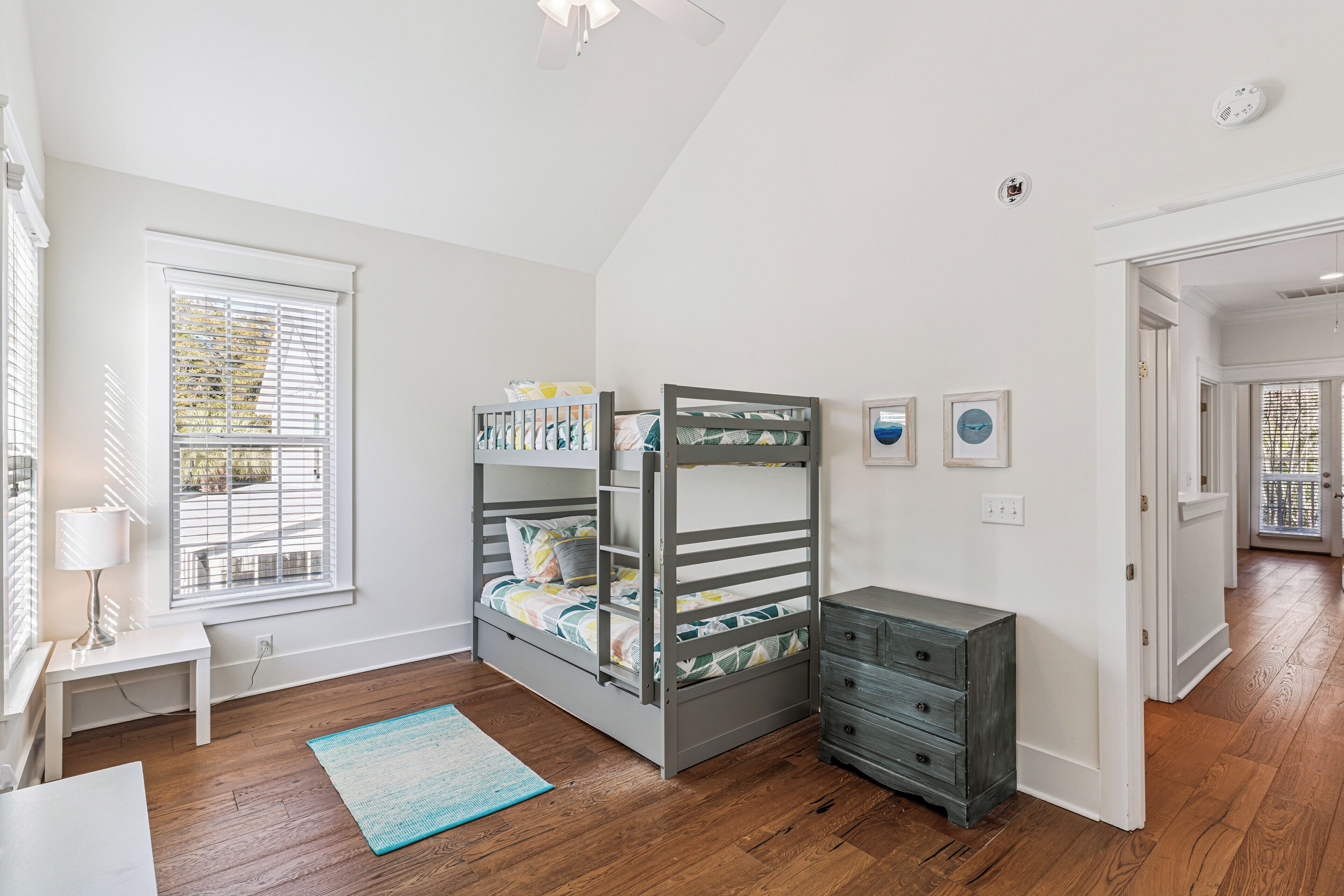 A child's bunk bed with a desk and dresser, a window with blinds, and a door leading to another room.