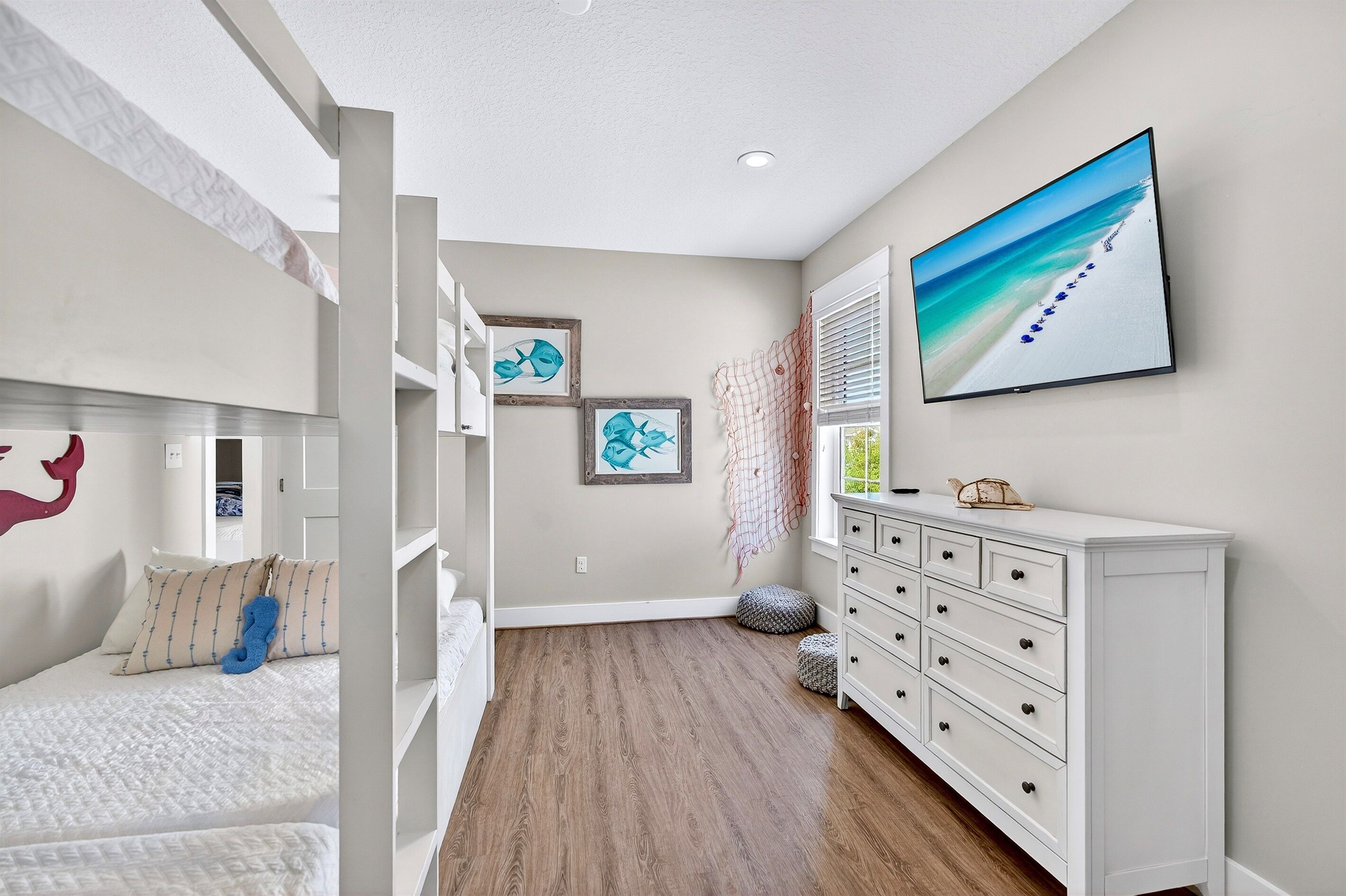 A bedroom with a bunk bed, a dresser, and a wall-mounted TV displaying a beach scene.