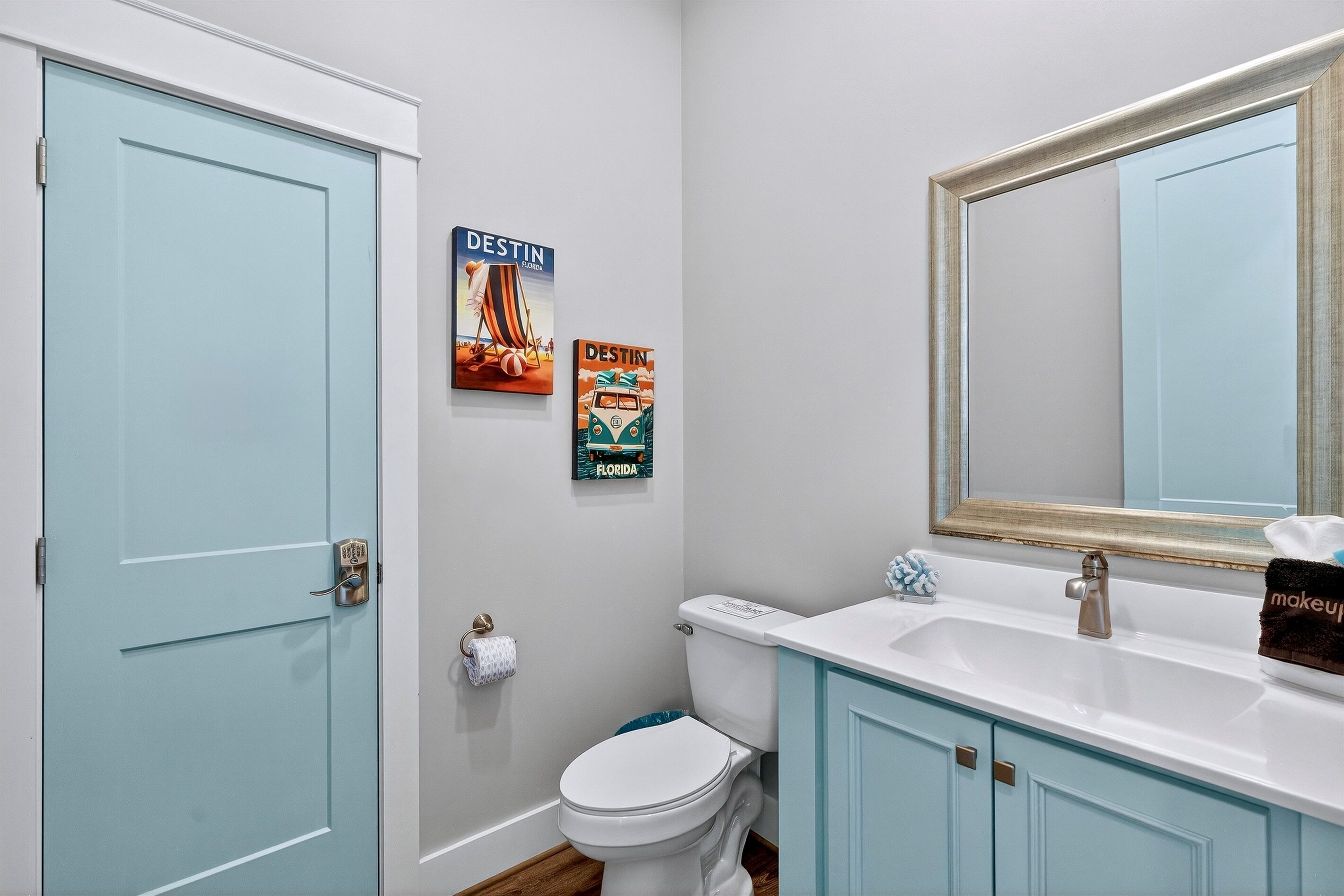 A bathroom with a white toilet, a sink with a mirror, and two posters on the wall.