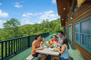 Un grupo de personas cenando en una terraza de madera con vistas a un paisaje boscoso.