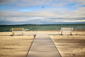 A wooden pathway leading to two benches on a sandy beach with the ocean in the background. - Mainstay in Elk Rapids, splendid views and comfort (Elk Rapids)