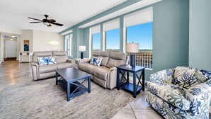 A spacious living room with a beige sofa, a patterned armchair, and a coffee table. There are large windows providing a view of the outdoors. - 🏖️Gulf Front - 2 Beachfront Pools - Great for Families - Seychelles 701🏖️ (Panama City)
