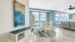 A dining area with a round table, chairs, a chandelier, and a view of the ocean through large windows. - 🏖️Gulf Front - 2 Beachfront Pools - Great for Families - Seychelles 701🏖️ (Panama City)
