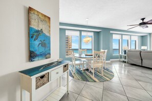 A dining area with a round table, chairs, a chandelier, and a view of the ocean through large windows. - 🏖️Gulf Front - 2 Beachfront Pools - Great for Families - Seychelles 701🏖️ (Panama City)