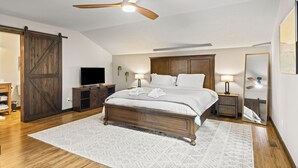 Une chambre avec un grand lit, un ventilateur de plafond, une télévision et une armoire.