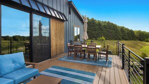 Une terrasse extérieure moderne dotée d’un espace repas, d’un canapé et offrant une vue sur un paysage boisé.