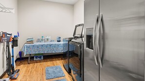 A compact kitchenette with a stainless steel refrigerator, a table with cleaning supplies, and a vacuum cleaner. - Wine Country Latitude. Northern Michigan Attitude (Suttons Bay)