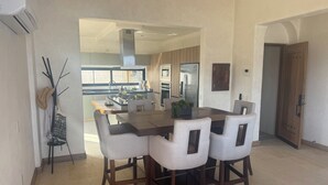 A dining area with a large table and four chairs, a kitchen in the background, and a ceiling fan. - Playa La Ropa 
Brand new Villa with 7-minute walk to the beach (Zihuatanejo)