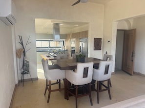 A dining area with a large table and four chairs, a kitchen in the background, and a ceiling fan. - Playa La Ropa 
Brand new Villa with 7-minute walk to the beach (Zihuatanejo)