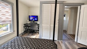 A hotel room with a bed, a desk with a computer, a television, and a sliding door leading to another room.