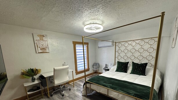 Een hemelbed met een groene plaid, een bureau met een stoel, een kleine plant en een raam met zonwering.