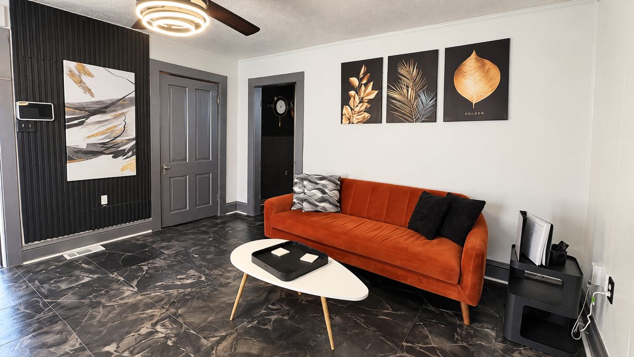 A modern living room with a dark wood panel wall, a black and white abstract painting, a red sofa, and a black coffee table.
