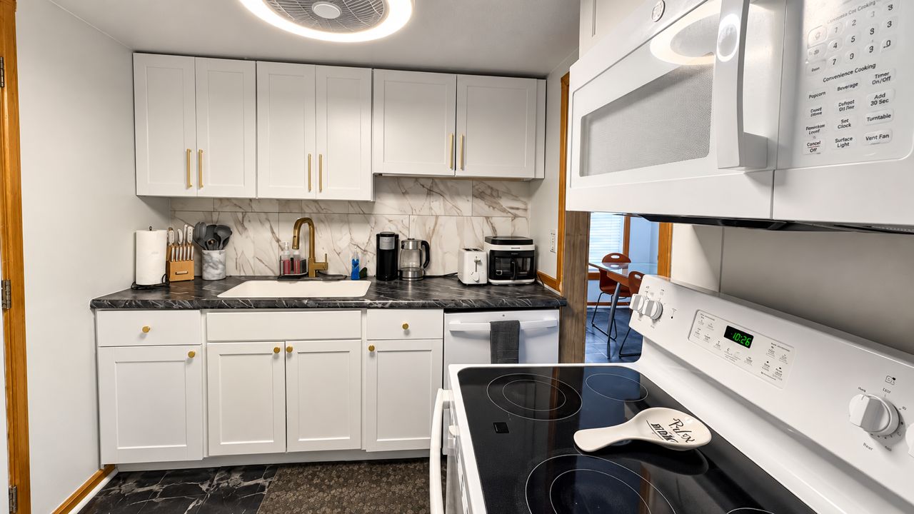 A kitchen with white cabinets, a black countertop, a stove, and a microwave.